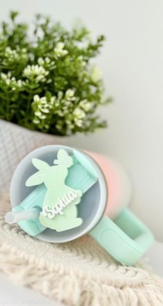 a cup with a bunny on it sitting next to a plant and some flowers in the background