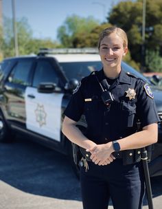 a woman police officer standing in front of her patrol car smiling for the camera,