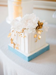 a white and blue wedding cake with gold flowers on the top is sitting on a table