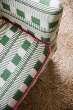 a green and white striped chair with pink piping on the armrests sitting on a rug