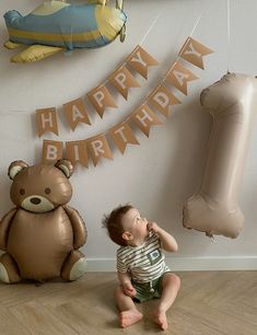 a baby sitting on the floor next to some balloons