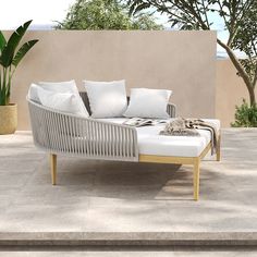 a white couch sitting on top of a cement floor next to a plant and potted tree