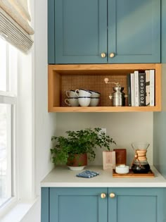 a kitchen with blue cupboards and white counter tops in the corner, next to a potted plant