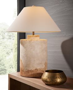 a table lamp sitting on top of a wooden shelf next to a vase and bowl