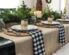 the table is set for christmas dinner with pine cones and greenery in jars on top