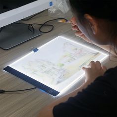 a woman is looking at a drawing on a light box that's lit up