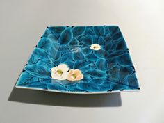 a blue plate with flowers on it sitting on a white counter top next to a gray wall