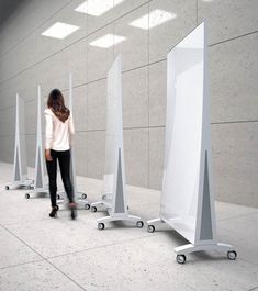 a woman is walking past several white poles in an empty room with light coming through the windows