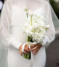 a woman in a white wedding dress holding a bouquet of flowers and wearing a veil