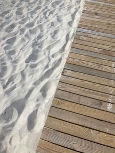 a wooden walkway leading to the beach with white sand and footprints in the sand on it