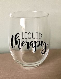 a wine glass with the words liquid therapy written in black ink on it sitting on a table