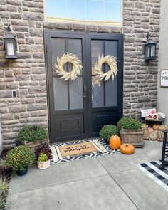 two wreaths on the front door of a house with pumpkins and other decorations