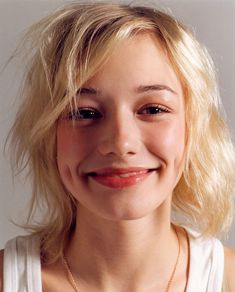 a close up of a person wearing a necklace and smiling at the camera with a smile on her face