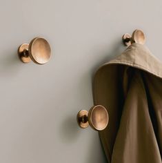 two coat hooks on the wall with coats hanging from it's back and one has an overcoat