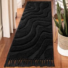 a black rug with fringes on the floor next to a potted plant