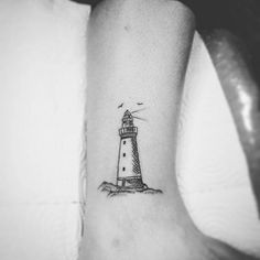 a black and white photo of a small lighthouse tattoo on the right inner arm,