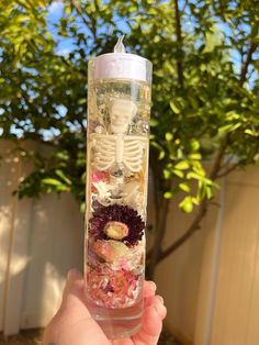 a person holding up a glass with flowers in it and a skeleton inside the tube