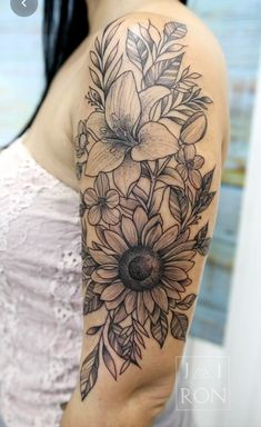 the back of a woman's shoulder with flowers and leaves tattooed on her arm