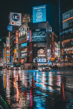 a wet city street at night with traffic lights and billboards on the buildings in the background