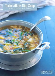 a metal bowl filled with soup on top of a blue tablecloth next to a spoon