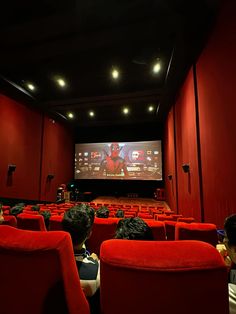 people sitting in red chairs watching a movie