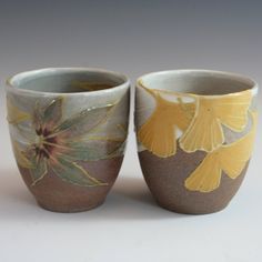 two vases with flowers painted on them sitting next to each other in front of a gray background