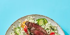 a white plate topped with meat, rice and veggies on top of a blue table