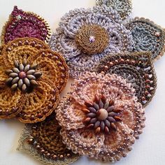 several crocheted flower brooches are arranged on a white tablecloth with beads