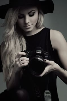 a woman with long blonde hair is holding a camera and wearing a black cowboy hat