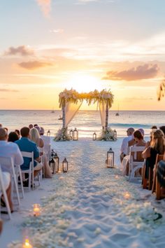 an outdoor wedding setup on the beach with candles lit up in front of it and people sitting at the end of the aisle