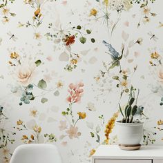 a white dresser sitting next to a wall covered in floral wallpaper and a potted plant