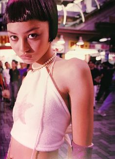 a woman with short black hair wearing a white top and pearls around her neck standing in front of a crowd