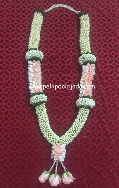 a green and white beaded necklace with flowers on it's end, sitting on a red surface