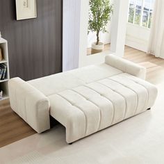 a white couch sitting on top of a hard wood floor next to a book shelf