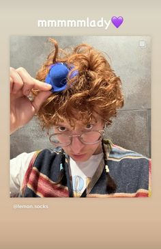 a person with curly hair and glasses holding a blue object in front of their face