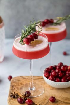 cranberry martini with rosemary garnish in coupe glasses on wooden cutting board