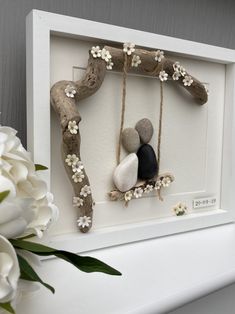 a white frame holding two rocks and flowers