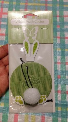 a hand holding a white and green cat toy in it's packaged package on a checkered table cloth