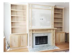 an empty living room with a fireplace and built in bookshelves