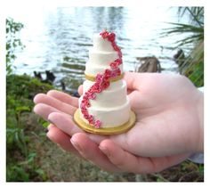 a hand holding a miniature wedding cake with pink flowers on it's top and bottom