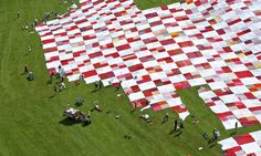 people standing around a giant quilt on the grass