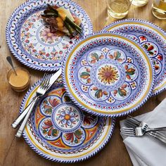 three plates with colorful designs on them sitting on a wooden table next to glasses and utensils