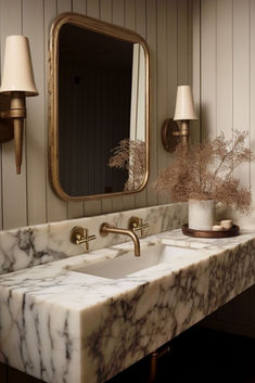 a bathroom with marble counter tops and gold fixtures, along with two wall sconces