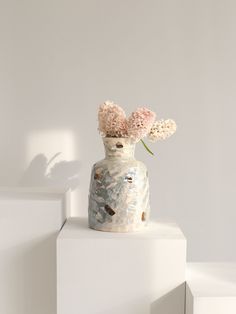 a white vase with pink flowers in it sitting on top of a block of concrete