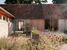 the house is made out of stone and has an outdoor patio area surrounded by wildflowers