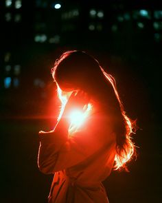 a woman standing in the dark holding her hand up to her face with bright light shining on her