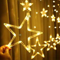 a hand is holding a star shaped string light in front of a curtain with stars hanging from it