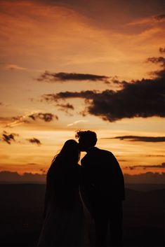 the silhouette of two people kissing in front of an orange and blue sky at sunset