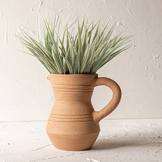 a plant in a clay vase on a white table with paint chipped walls behind it