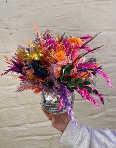 a person holding a disco ball filled with colorful flowers and feathers in front of a white brick wall